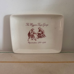 May include: White ceramic dish with a brown image of two people making paper. The text reads "The Wiggins Teape Group Papermakers 1701-1961".