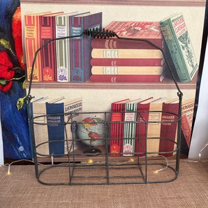 May include: A black metal wire bottle carrier with a spring handle. The carrier has six compartments for holding bottles. The carrier is sitting on a brown burlap surface.