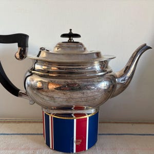 Peut inclure: Théière en argent avec une poignée noire et un socle rayé bleu, rouge et blanc.