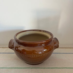 May include: A brown ceramic pot with two handles. The pot has a glazed finish and a beaded design around the rim.