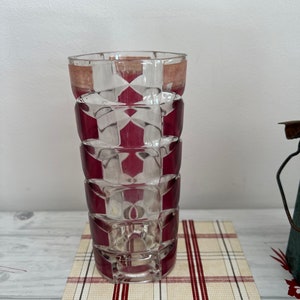 Könnte beinhalten: Eine klare Glasvase mit einem geometrischen Muster aus burgunderroten Quadraten. Die Vase steht auf einer rot-weiß karierten Oberfläche.