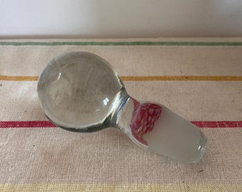 May include: A clear glass bottle stopper with a red and white patterned design.