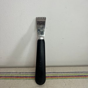 Puede incluir: Un rallador de cítricos plateado con un mango de plástico negro. El rallador tiene un borde dentado y se utiliza para rallar cítricos.