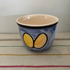 Może przedstawiać: Mały, niebieski kubek ceramiczny z czarną obwódką i żółto-pomarańczowym wzorem. Kubek jest ręcznie malowany prostym wzorem dwóch żółto-pomarańczowych kształtów.