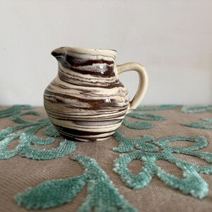 Pode incluir: Um conjunto de três canecas de cerâmica com acabamento fosco e salpicado. As canecas são em tons de creme, cinza claro e cinza escuro. Cada caneca tem um design simples e minimalista.