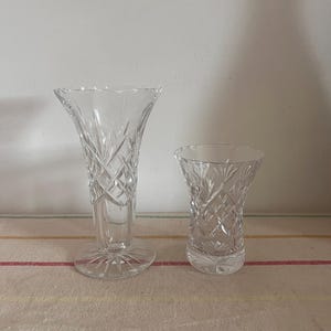Op de afbeelding: Twee heldere glazen vazen met een diamantpatroon. De grotere vaas is hoger en heeft een bredere basis. De kleinere vaas is lager en heeft een smallere basis.