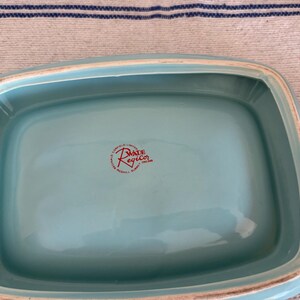 May include: A rectangular, light turquoise ceramic dish with a slightly raised rim. The dish has a glossy finish and a red stamp that reads "MADE RegicO ENGLAND". The dish is likely vintage.