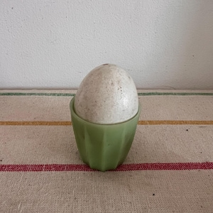 Puede incluir: Un huevo blanco moteado en un huevo de color verde en un mantel a rayas.