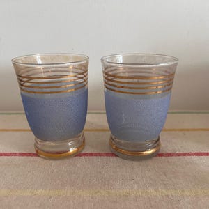 Puede incluir: Dos vasos de chupito de vidrio transparente con un acabado azul esmerilado y bandas doradas alrededor del centro.