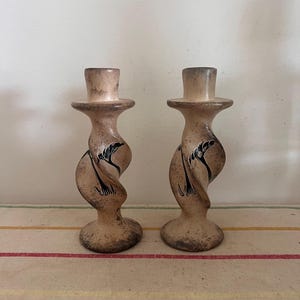 May include: A pair of brown and black candle holders with a twisted design and floral carvings. The candle holders are made of soapstone.