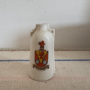 Puede incluir: Tapón de botella de cerámica blanca con un escudo rojo y amarillo con un león y el texto "Do Well Doubt Not".