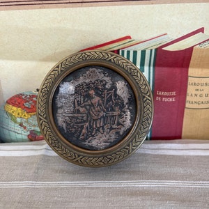 A French antique brass tin with a lady watering in a garden with a dog at her feet