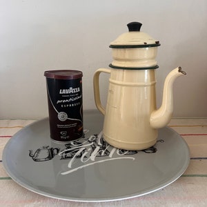 May include: A white enamel coffee pot with a black lid and green trim sits on a gray tray with the word "Coffee Time" printed on it. A can of Lavazza Prontissimo Espresso coffee is also on the tray.