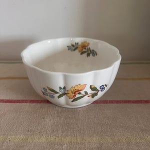 May include: A white ceramic bowl with a scalloped rim and a floral design featuring yellow, orange, blue, and green flowers.