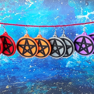 May include: Six pairs of earrings with a black pentagram design. The earrings are in red, orange, gray, and purple.