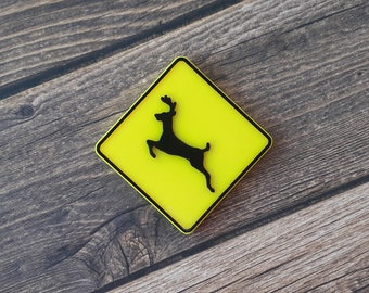 May include: Yellow diamond-shaped warning sign with a black silhouette of a deer jumping. The sign has a black border.