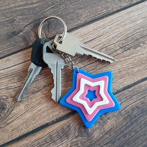 May include: A silver key chain with three keys and a blue, pink, and white star-shaped charm.