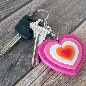 May include: A pink, white and orange layered heart keyring with two keys attached.