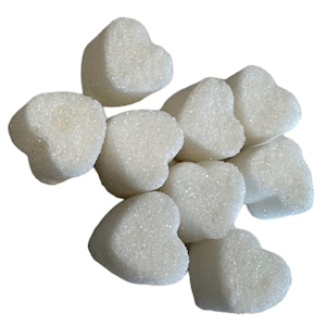 May include: A cluster of heart-shaped sugar cubes. The cubes are white and have a slightly textured, granulated surface. The shapes are irregular, with rounded edges, and are scattered against a white background.