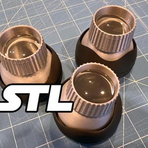 Puede incluir: Tres lupas plateadas y negras con lentes transparentes están dispuestas sobre una superficie de cuadrícula azul. El texto "STL" se muestra en letras blancas en la esquina inferior izquierda.