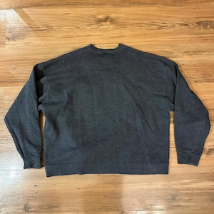 K&ouml;nnte beinhalten: Ein dunkelgraues Sweatshirt mit Rundhalsausschnitt und langen &Auml;rmeln. Das Sweatshirt besteht aus einem weichen Material und hat gerippte B&uuml;ndchen und Saum. Das Kleidungsst&uuml;ck liegt flach auf einer Holzoberfl&auml;che.