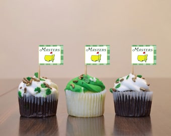 May include: Three cupcakes decorated with green and white frosting and gold sprinkles. Each cupcake has a toothpick with a green and white flag that says "Masters" with a yellow and red golf flag on it.