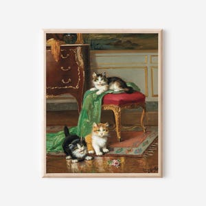 May include: A framed print of an antique painting featuring three kittens. One kitten rests on a red stool draped with green fabric, while two others sit on the floor. The artwork has a classical style with a detailed interior setting.