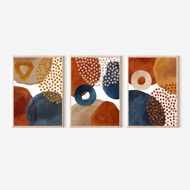 May include: Set of three framed abstract art prints. Each print features watercolor-style shapes in rust, navy blue, tan, and gold, with dotted and solid elements. The artwork has a modern, minimalist aesthetic.