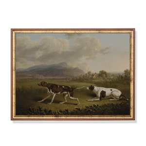 Op de afbeelding: Een schilderij van twee bruine en witte jachthonden in een veld. De hond op de voorgrond rent, terwijl de hond op de achtergrond ligt. Het schilderij is geschilderd tegen een achtergrond van glooiende heuvels en een bewolkte lucht.