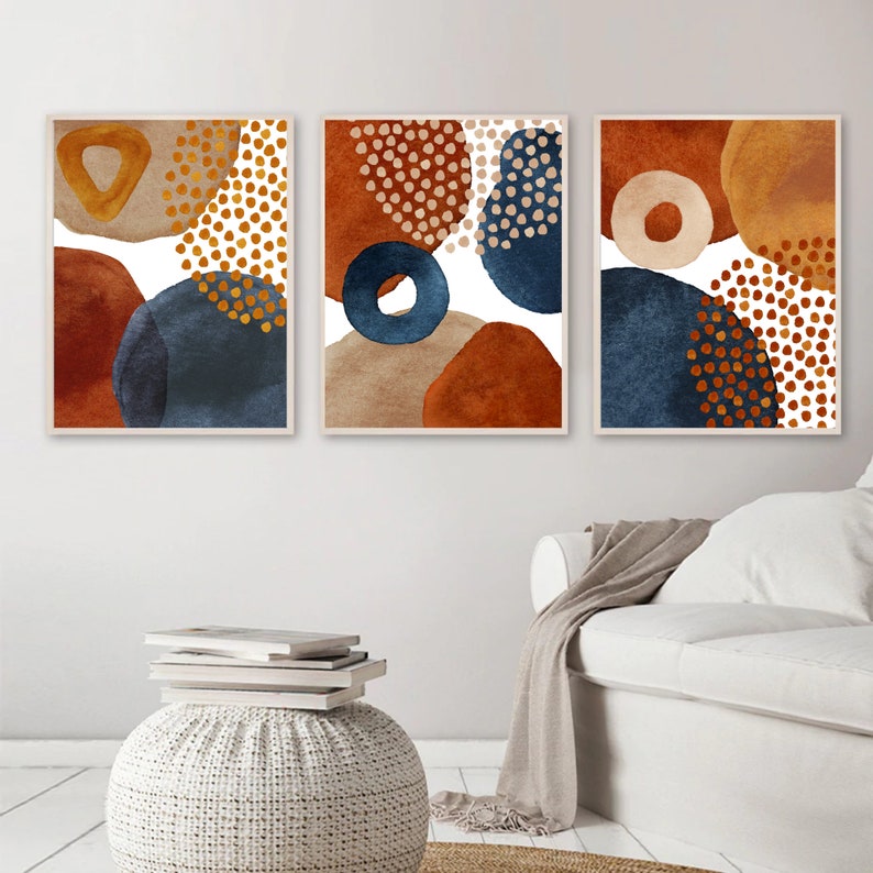 May include: Three framed abstract art prints. Each print features a unique arrangement of organic shapes in shades of rust, navy blue, beige, and gold. The designs include circles, dots, and irregular forms, creating a modern and artistic aesthetic.