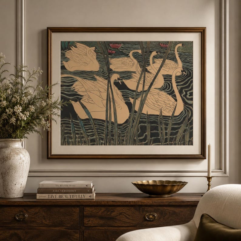May include: A framed wall art print featuring a stylized illustration of several beige swans swimming in dark water with tall green reeds and small pink water lilies. The artwork is enclosed in a dark brown wooden frame with a wide white mat border.