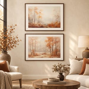 May include: Two rectangular landscape paintings in dark brown frames featuring a misty forest scene with autumn-toned trees in shades of orange, rust, and muted beige, displayed vertically one above the other on a neutral-coloured wall.