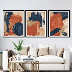 May include: Three abstract art prints with a modern minimalist design. The prints feature bold brushstrokes in shades of blue, orange, and gold on a cream background.