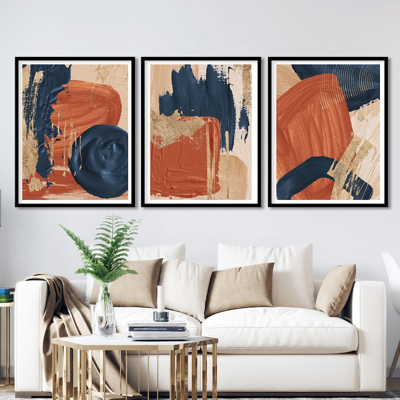 May include: Three abstract art prints with a modern minimalist design. The prints feature bold brushstrokes in shades of blue, orange, and gold on a cream background.