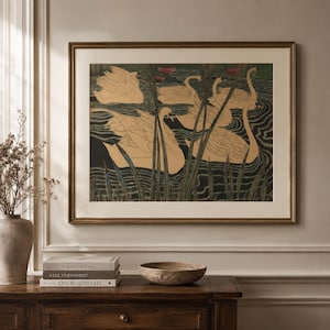May include: A framed wall art print featuring a stylized illustration of several beige swans swimming in dark water with tall green reeds and small pink water lilies. The artwork is enclosed in a thin metallic frame with a wide off-white mat border.