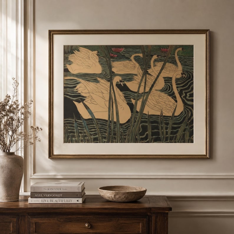May include: A framed wall art print featuring a stylized illustration of several beige swans swimming in dark water with tall green reeds and small pink water lilies. The artwork is enclosed in a thin metallic frame with a wide off-white mat border.