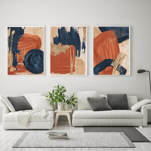 May include: Three abstract art prints with a modern minimalist design. The prints feature a combination of blue, orange, and gold paint strokes on a beige background.