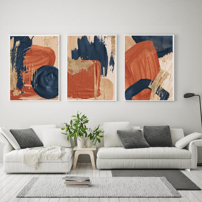 May include: Three abstract art prints with a modern minimalist design. The prints feature a combination of blue, orange, and gold paint strokes on a beige background.