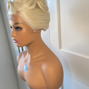 May include: A blonde wig with a high updo style on a mannequin head. The wig is styled in a classic updo with a smooth finish.
