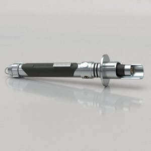 Puede incluir: Un sable de luz plateado y negro con un mango negro y una hoja plateada. La hoja está retraída y el sable de luz está sobre una superficie blanca.