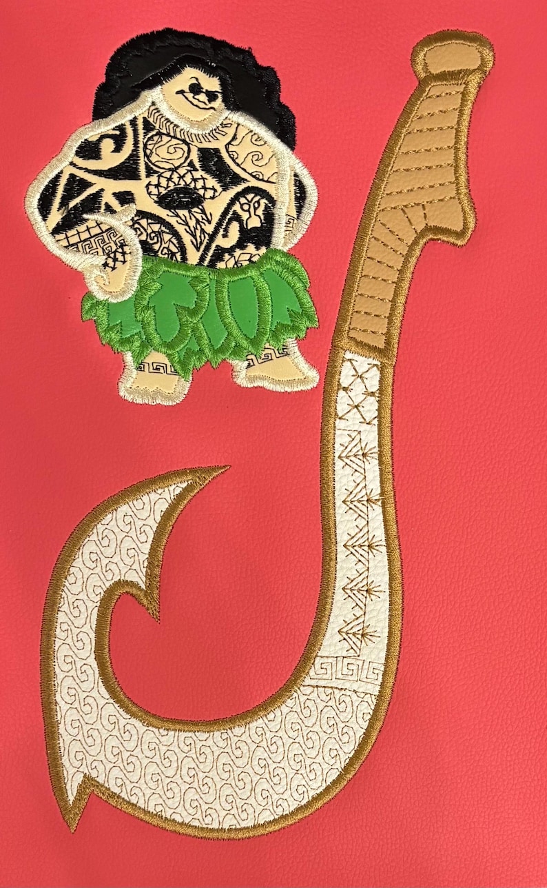 May include: Embroidered design featuring a cartoon figure with tattoos and a green grass skirt, alongside a large, curved hook. The hook and figure are in shades of tan, white, and gold, set against a red background.