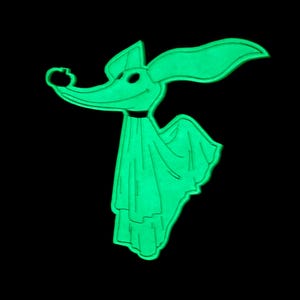 Puede incluir: Un personaje de perro fantasma de dibujos animados verde brillante con orejas grandes, una nariz larga y un collar negro. El personaje lleva una s&aacute;bana drapeada y tiene una expresi&oacute;n sonriente. El fondo es negro s&oacute;lido.