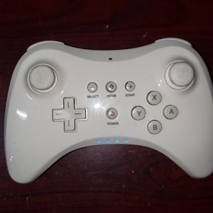 May include: White wireless video game controller with buttons labeled 'A', 'B', 'X', 'Y', 'Home', 'Start', 'Select', and 'Power'.