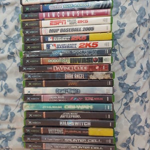 May include: A stack of Xbox video game cases. Titles include "Double War", "Ultra Bust-A-Move", "Namco Museum", "ESPN College Hoops 2K5", "Star Wars Battlefront", and "Tom Clancy's Splinter Cell". The cases are in various colors.