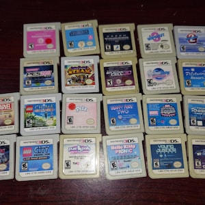 May include: A collection of 18 Nintendo 3DS game cartridges, featuring a variety of titles including LEGO Marvel Super Heroes, Chima, and Hello Kitty Picnic. The cartridges are arranged in three rows of six, with the titles visible on each cartridge.