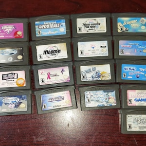 May include: A collection of 20 video game cartridges for the Nintendo DS handheld gaming system. The cartridges are arranged in rows and are all black with colorful labels. Some of the games include "World Poker Tour", "Madden NFL 2005", "Shrek 2", and "Kids Cards".