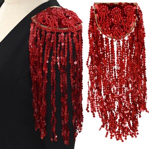 May include: Red sequined shoulder piece with a fringe of sequins. The piece is shaped like a curved rectangle and has a gold trim.