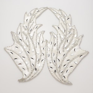 May include: A pair of white fabric appliques shaped like stylized leaves or wings, heavily embellished with silver-toned beads, clear rhinestones, and reflective silver sequins arranged in a detailed, symmetrical pattern across the surface.