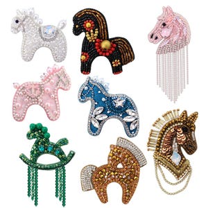 Könnte beinhalten: Eine Sammlung von Pferdebroschen aus Perlen in verschiedenen Farben und Designs. Die Broschen umfassen ein weißes Pferd mit Kristallakzent, ein schwarzes Pferd mit roten und goldenen Details und ein rosa Pferd mit Perlenakzenten. Weitere Farben sind Blau, Grün und Braun.