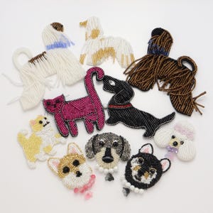 May include: A collection of beaded animal patches featuring various dog and cat designs. The assortment includes full-body figures of white, brown, and black dogs, a pink cat, and a yellow cat, alongside detailed head-only patches of dogs.